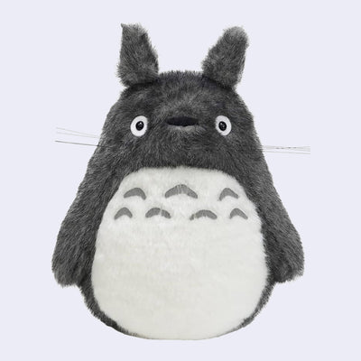 Dark gray Totoro plush, with a large white furry belly and whiskers. He has no mouth.