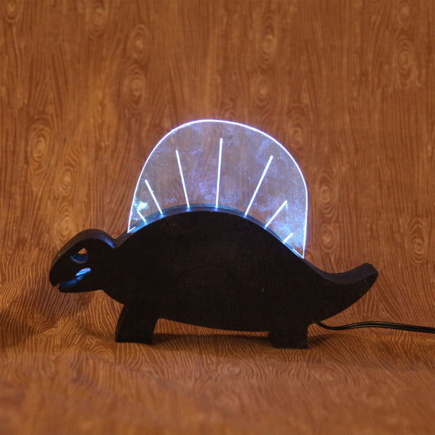 Wooden sculpture of a black dinosaur, flat mostly and emphasizing its silhouette.  Atop its back is a rounded plastic sheet with a line of lights, illuminating it and the interior of its mouth.