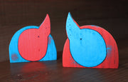 Back view of 2 painted die cut wooden dinosaur sculptures. Their tails are pointed up and they have small 'x's for buttholes.