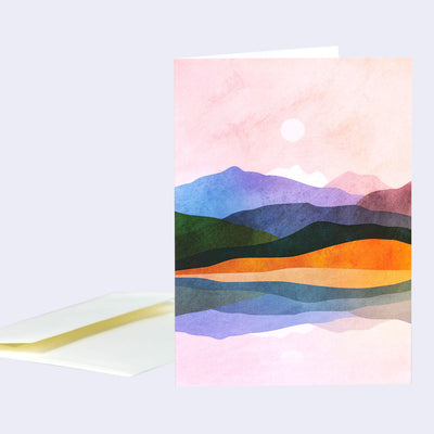 Greeting card with an illustration of a pink sky landscape over several rows of simplistic, colorful mountains.