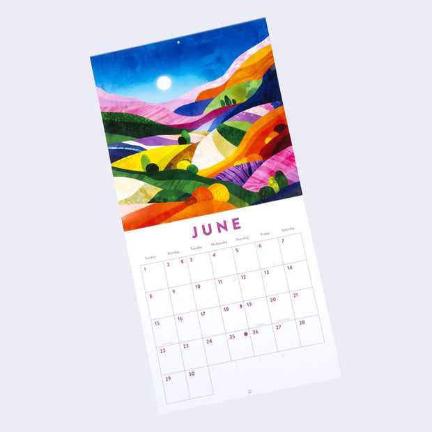 Staple bound calendar for the month of June, with one page being a full bleed illustration and the other having space for writing in each day. Illustration is of a sunset landscape with many colorful rolling hills and stylized simple trees.