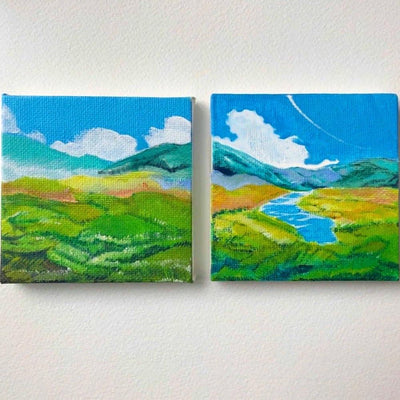 2 small painted canvases of one continuous image, in a diptych style of a lush green landscape in front of tall mountains and a blue sky with white fluffy clouds.