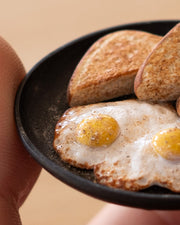 Small assembled clay sculpture of a breakfast on a plate of eggs, toast and 2 links of sausage.  Close up to show detail.