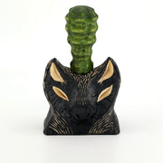 Whittled wooden sculpture of the bust of a bat/wolf creature, black with wooden accents. Coming out of its head is a green bumpy succulent cactus.