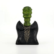 Whittled wooden sculpture of the bust of a bat/wolf creature, black with wooden accents. Coming out of its head is a green bumpy succulent cactus.