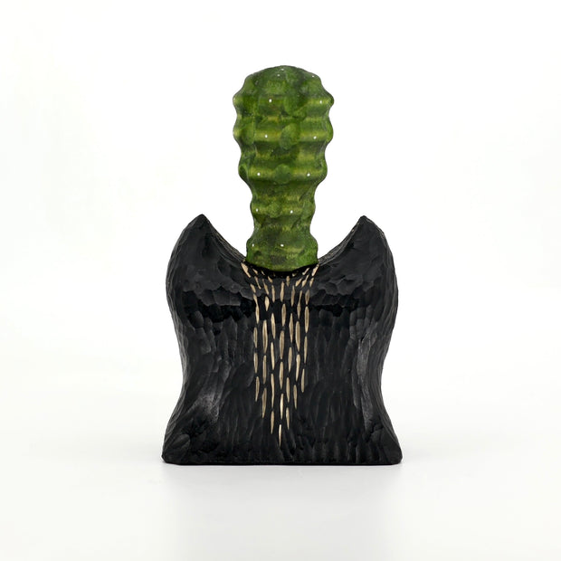 Whittled wooden sculpture of the bust of a bat/wolf creature, black with wooden accents. Coming out of its head is a green bumpy succulent cactus.