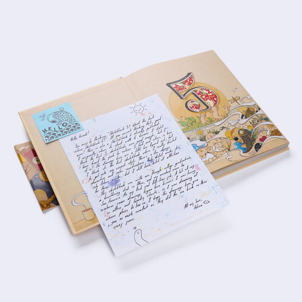 Open view of the front cover interior, with a loose sheet of paper with a written note by Felicia Chiao. Front page is a colorful illustration under the large number 5.