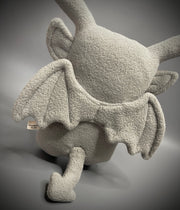 Plush doll of a bunny with skinny ears and a flat body, made to look like a gargoyle. It holds a pleather flower and plucks a petal from it.