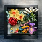 Ceramic sculpture in an open shadow box frame featuring many flowers, alike to the ones from Alice in Wonderland. A small blonde girl stands off to the side and looks onward with her back facing the viewer.