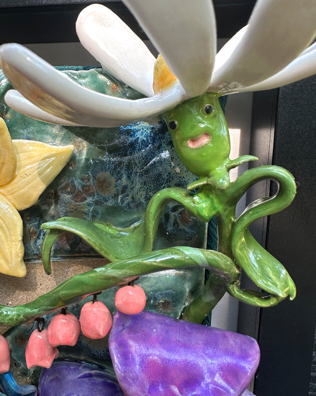 Ceramic sculpture in an open shadow box frame featuring many flowers, alike to the ones from Alice in Wonderland. A small blonde girl stands off to the side and looks onward with her back facing the viewer.