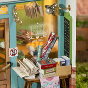 Assembled diorama of a miniature bookshop, with lights on inside and books visible from the windows. Outside are various sale items and wrapping paper.