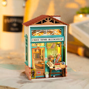 Assembled diorama of a miniature bookshop, with lights on inside and books visible from the windows. Outside are various sale items and wrapping paper.