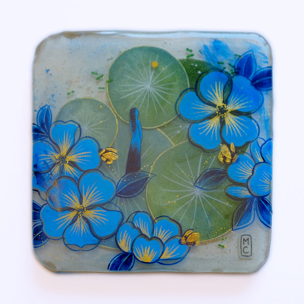 Resin coated square featuring green lilypads and blue and gold flowers. A slender blue woman stands in the middle and looks off, with gold bees buzzing around.