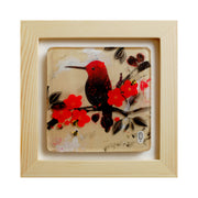 Illustration of a black and red hummingbird sitting on a branch with red flower blossoms and black leaves. A small silhouetted woman sits on the branch and looks onwards. Piece in open frame.