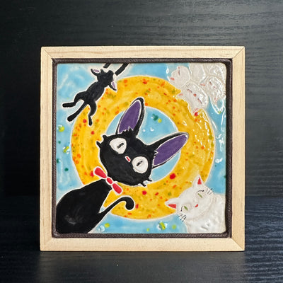 Ceramic tile light blue with a yellow circle. Each corner has a cat character: Jiji from Kiki's Delivery Service, the white cat from Kiki's Delivery Service and their kittens.