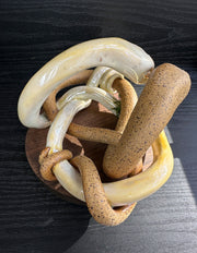 Ceramic sculpture of 2 brown snakes, intertwined with one another. One is matte brown like sand and the other is a glossy yellow. They both have golden eyes and their faces pressed together.