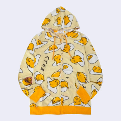 Light yellow hooded jacket with a repeating all over pattern of Gudetama, sitting on egg yolk, inside of an egg shell or wrapped in bacon. 