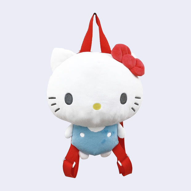 Plush doll of Hello Kitty, with her iconic red bow and blue overalls, made into a backpack with red straps and a zip atop the back of her head.