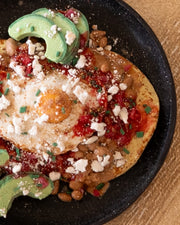 Small assembled clay sculpture of a model breakfast on a plate of huevos rancheros: eggs atop of tortillas with avocado, pico de gallo, pinto beans and cotija cheese.