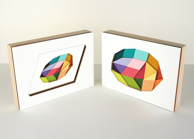 2 artworks comprised of several layers of cut paper, revealing geometric shapes of many colors within a larger single geometric shape. Pieces are mounted to wood and sit beside one another.