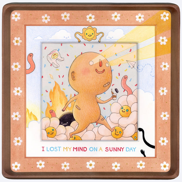 Drawing inside a rounded corner wooden frame of a nude, round headed light tan character walking with bandaids on and shooting light beams out of its eyes. Around it is a chaotic setting of cartoon flowers, confetti and a fire. The mat around the piece is drawn on with various doodles.