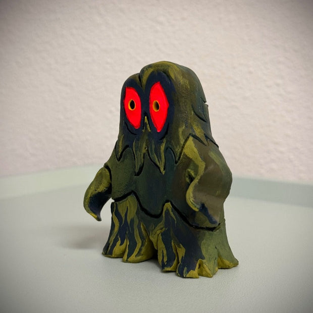 Sculpture of Hedorah, a pollution smoke monster, dark blue and yellowish green. It stands on 2 slimey legs and has large red eyes.