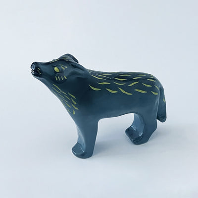 Ceramic sculpture of a bluish black wolf, standing and howling at the moon. Its two pairs of legs (front and back respectively) are paired together and it has gold eyes and fur color accents.