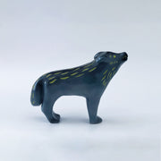 Ceramic sculpture of a bluish black wolf, standing and howling at the moon. Its two pairs of legs (front and back respectively) are paired together and it has gold eyes and fur color accents.