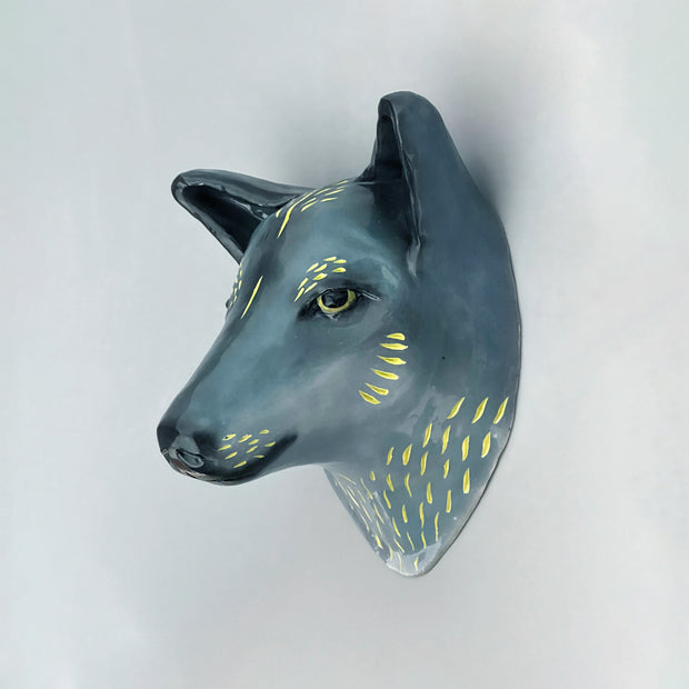 Ceramic sculpture of the bust of a blue wolf, with gold fur highlights and a serious, closed mouth expression.