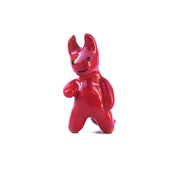 Glazed ceramic sculpture of a red devil with soft edged horns and a simple drawn on smile. It has rounded limbs and extends one arm out.