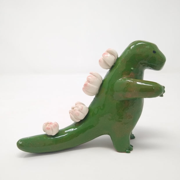 Glazed ceramic sculpture of a green Godzilla figure with lotus flower instead of back spikes. It reaches one hand out.