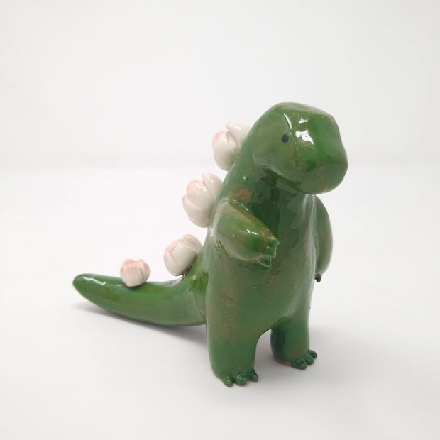 Glazed ceramic sculpture of a green Godzilla figure with lotus flower instead of back spikes. It reaches one hand out.