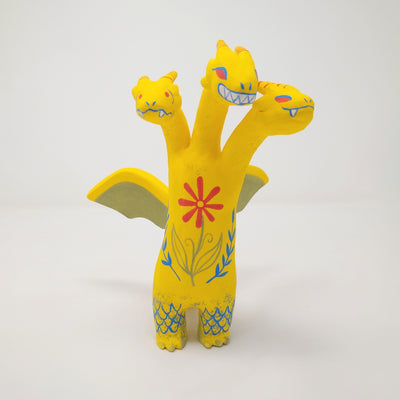 Sculpture of King Ghidorah, with 3 long necks and a set of small wings. It is painted yellow with a floral motif on its stomach. Each face has a different expression.