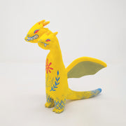 Sculpture of King Ghidorah, with 3 long necks and a set of small wings. It is painted yellow with a floral motif on its stomach. Each face has a different expression.