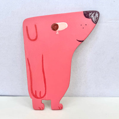 Cut out flat wooden sculpture of a pink dog, looking off to the side with a single tear falling. It has a shiny nose and small smile.