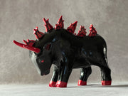 Black ceramic sculpture of a bull, faced down with an angry expression and red color accents for its eyes, horns, hooves and mane. Atop its back are red flames in place of a mane.