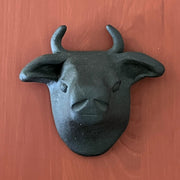 Black matte clay sculpture of a bull's head mounted onto the wall and flat on the back.