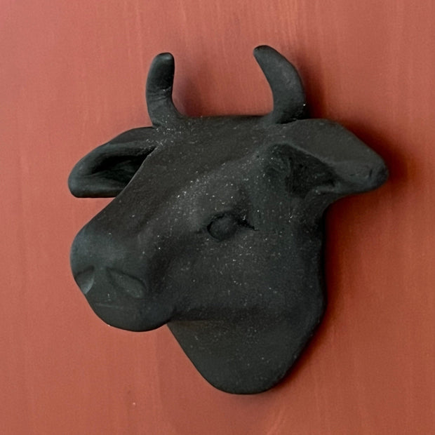 Black matte clay sculpture of a bull's head mounted onto the wall and flat on the back.