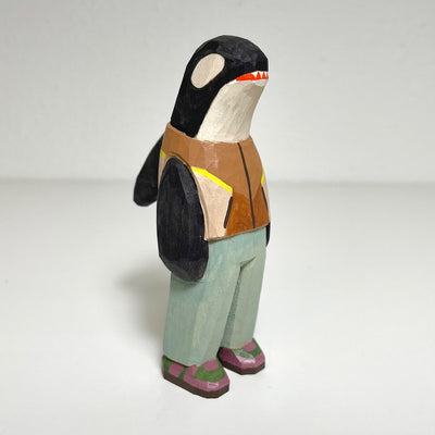 Carved and painted wooden sculpture of an orca, standing up on 2 legs like a person. It wears a brown vest, light blue pants and purple and green sneakers.