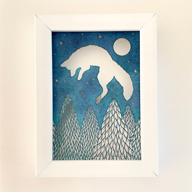 Blue paper with cut out imagery of a jumping fox, which leaps over a row of cut out pine trees. In the top right corner is a full moon and smaller stars.