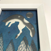 Blue paper with cut out imagery of a jumping fox, which leaps over a row of cut out pine trees. In the top right corner is a full moon and smaller stars.