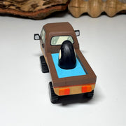 Painted small whittled wooden sculpture of a brown striped pick up truck, with the pick up filled with water. The head of a killer whale peeks out from the water.