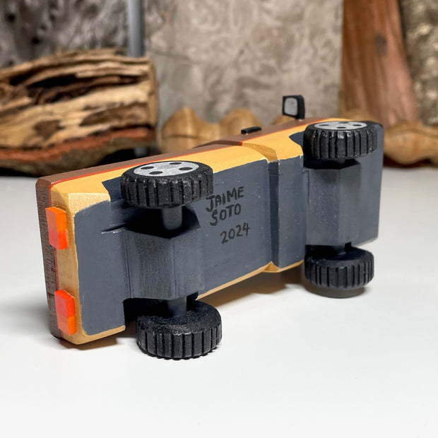 Painted small whittled wooden sculpture of a brown striped pick up truck, with the pick up filled with water. The head of a killer whale peeks out from the water.