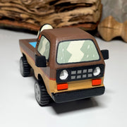 Painted small whittled wooden sculpture of a brown striped pick up truck, with the pick up filled with water. The head of a killer whale peeks out from the water.