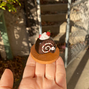 Small sculpture of a snake shaped like a chocolate swiss roll with strawberry cream filling. The snake's head comes out of the cake swirl and has a dollop of whipped cream. Atop the snake's back is a larger dollop of whipped cream with strawberries.