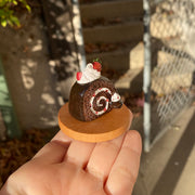 Small sculpture of a snake shaped like a chocolate swiss roll with strawberry cream filling. The snake's head comes out of the cake swirl and has a dollop of whipped cream. Atop the snake's back is a larger dollop of whipped cream with strawberries.