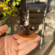 Small sculpture of a snake shaped like a chocolate swiss roll with strawberry cream filling. The snake's head comes out of the cake swirl and has a dollop of whipped cream. Atop the snake's back is a larger dollop of whipped cream with strawberries.