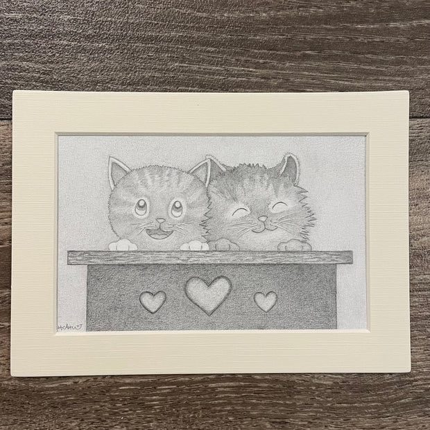 Framed graphite illustration of 2 cute cartoon cats sitting in a box with hearts on the exterior.