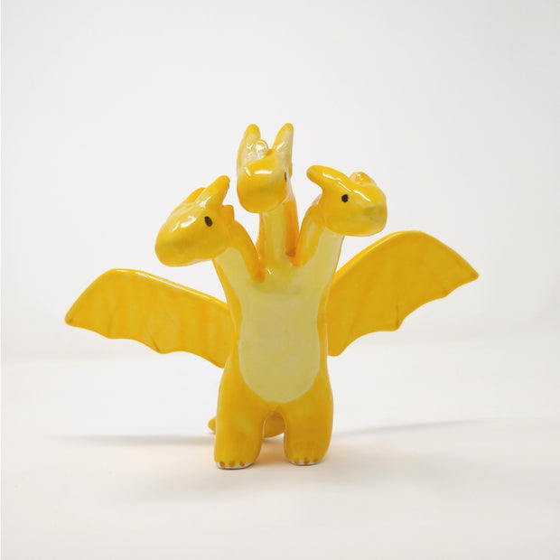 Yellow glazed ceramic sculpture of a 3 headed dragon, with wings spread out. The heads each have soft horns and minimal facial features, with only eyes.