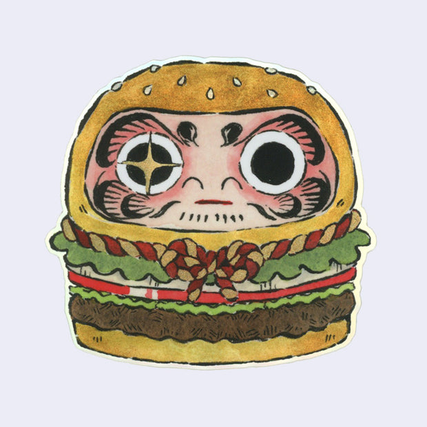 Die cut sticker of a burger shaped to look like a Japanese daruma doll with a gold and red braided rope around the center.